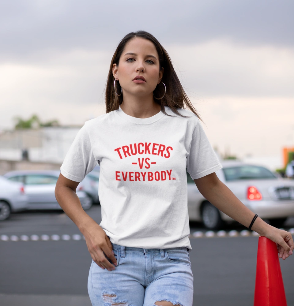 Woman wearing white Truckers VS Everybody t-shirt, standing in a parking lot with her hands on a red traffic cone